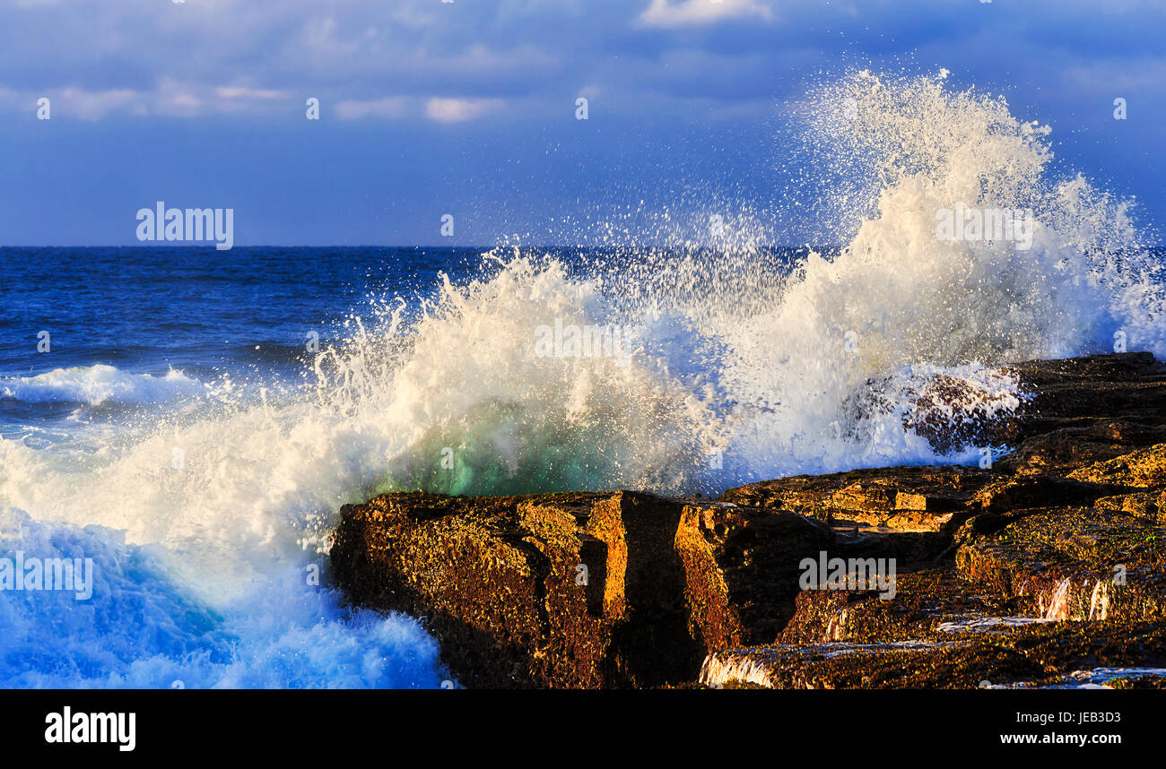 Una forte ondata di rotolamento hits rocce di arenaria della costa del Pacifico in Australia su una mattina di sole contro il cielo blu e il mare aperto orizzonte. Foto Stock