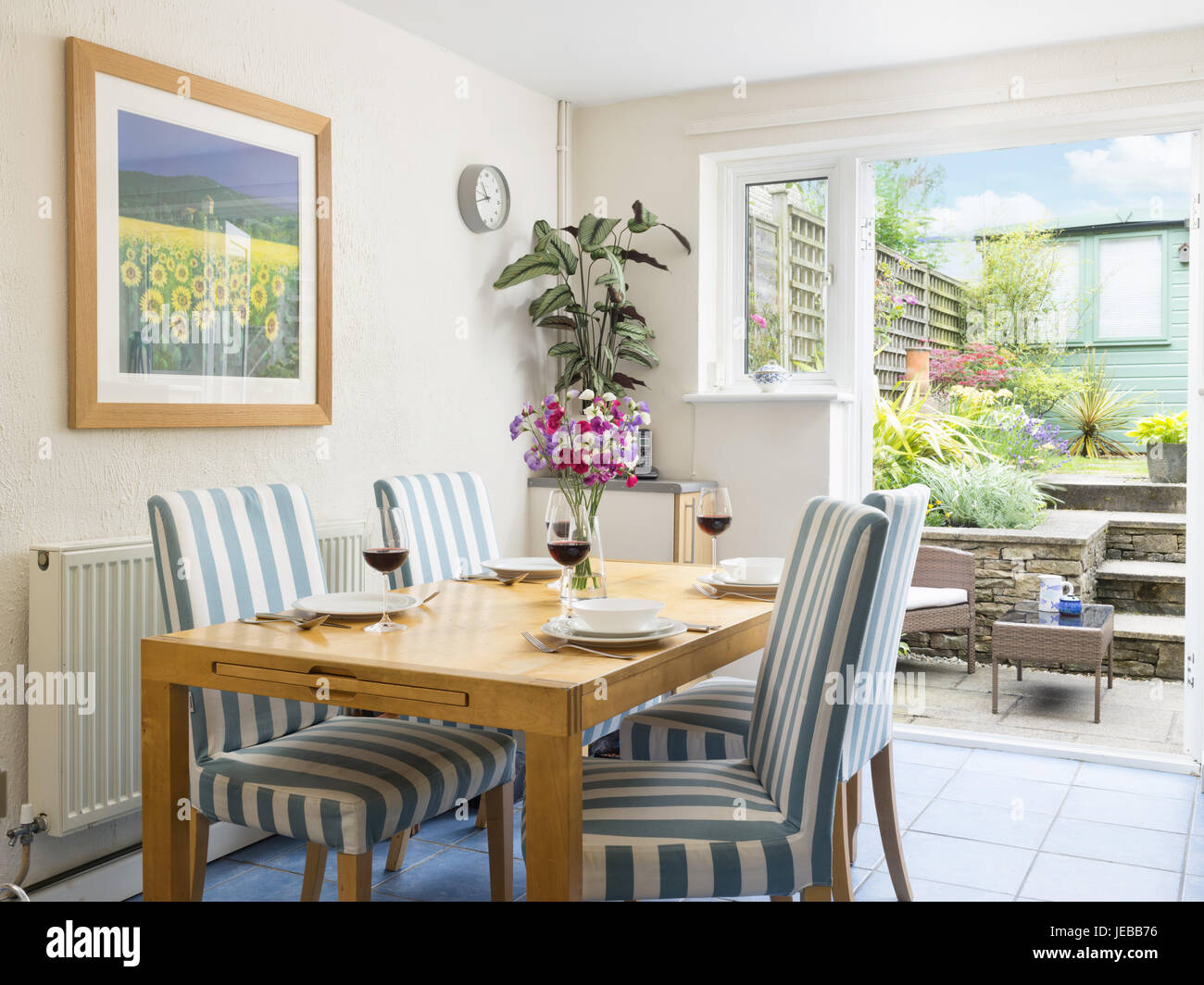 Un tavolo da pranzo prevista per un pasto & sedie in una piccola sensazione fresca sala da pranzo con un patio aperto porte che conducono ad un piccolo cortile con giardino Foto Stock