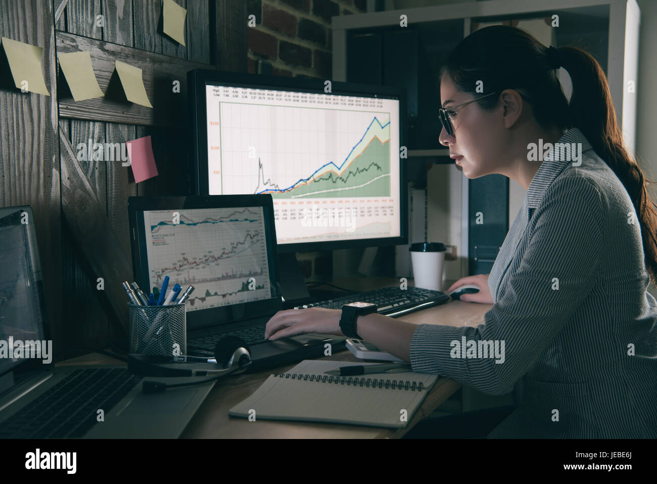 Indossare occhiali analisti finanziari ricerca grafico più recente in un ufficio moderno. asia donna che lavorano di notte catturare nuove notizie finanziarie. Foto Stock