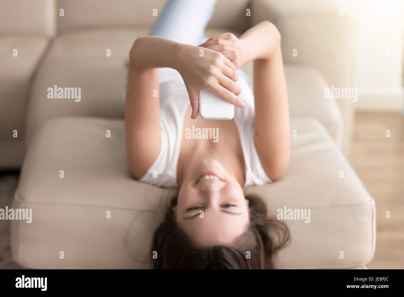 Felice giovane donna utilizzando il cellulare sul divano di casa Foto Stock