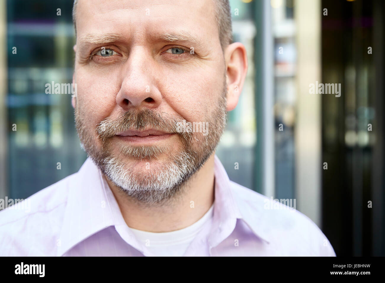 Headshot ritratto di uomo di mezza età in maglia rosa. Egli è in piedi di fronte al suo ufficio. Foto Stock
