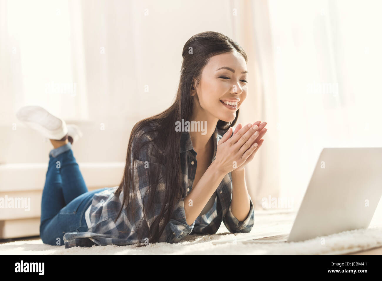 Felice donna sdraiata sulla moquette e battendo le mani nella parte anteriore del computer portatile Foto Stock