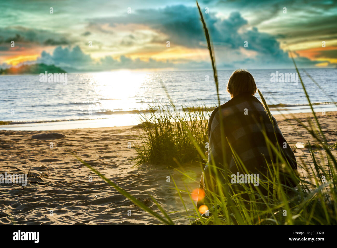 Silhouette di donna senior seduto da solo nella spiaggia di fronte al mare Foto Stock