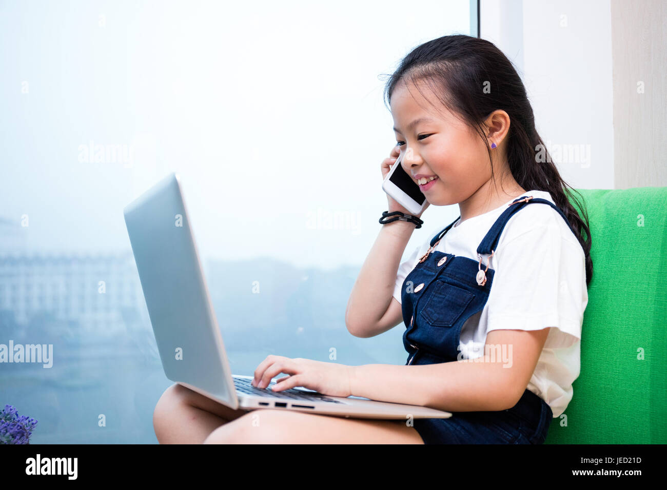 Cinese asiatici bambina a parlare al telefono con il computer portatile sul  davanzale di casa Foto stock - Alamy