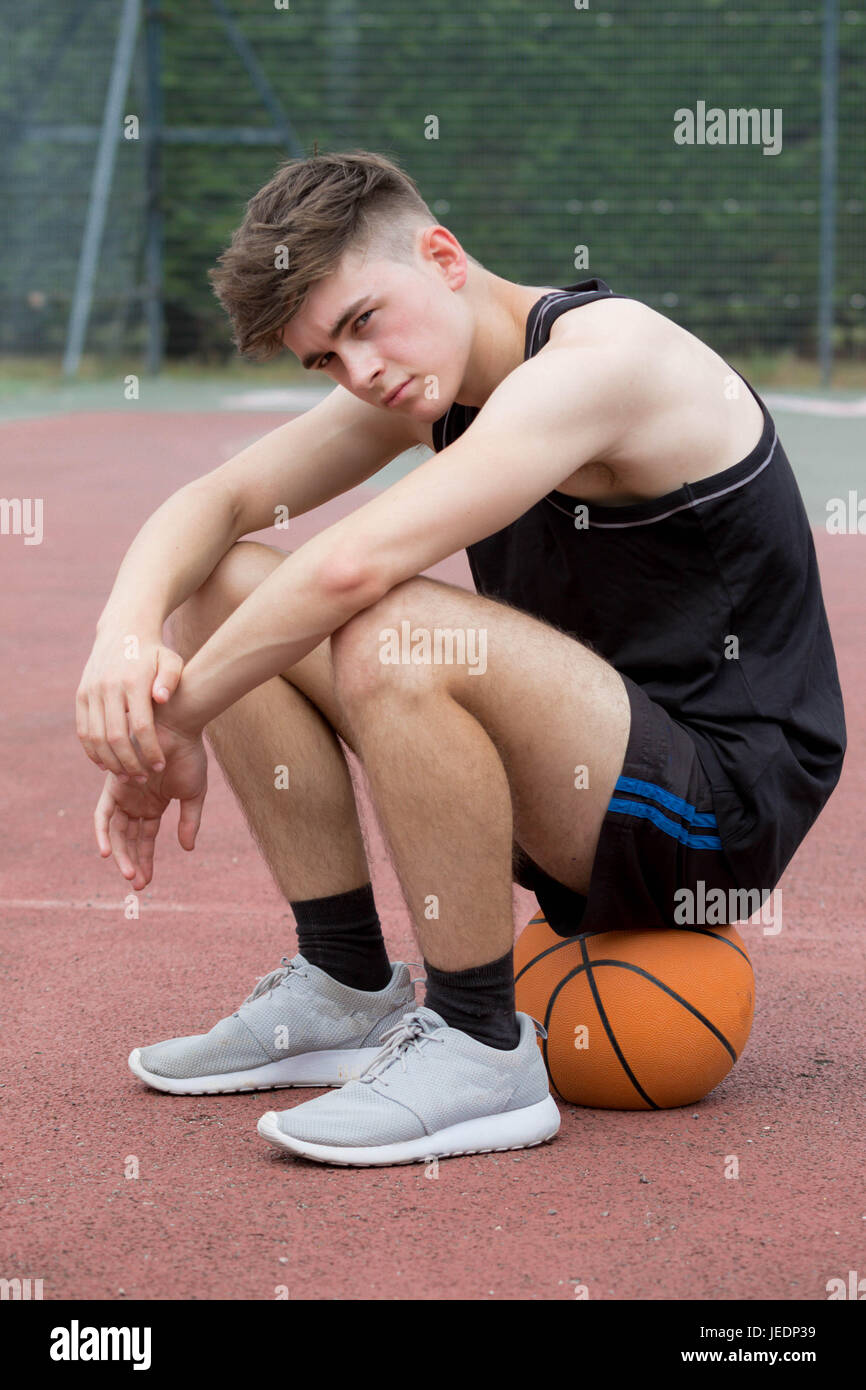 Ragazzo adolescente seduto su una palla da basket su una corte cercando  triste Foto stock - Alamy