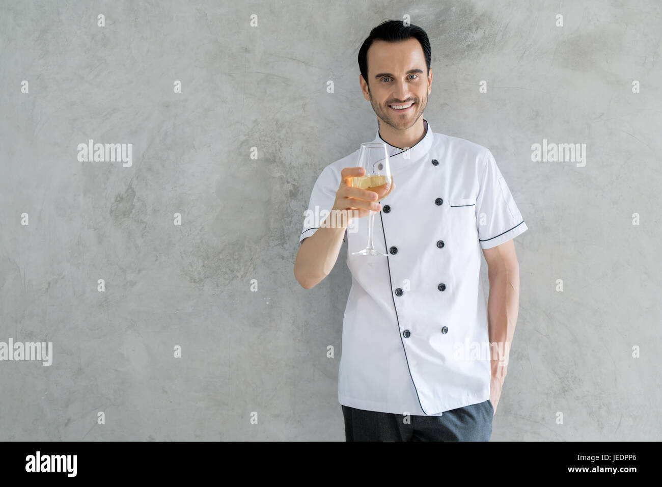 Ritratto di uomo caucasico cuocere tenendo un bicchiere di vino bianco. Girato nel ristorante. Foto Stock