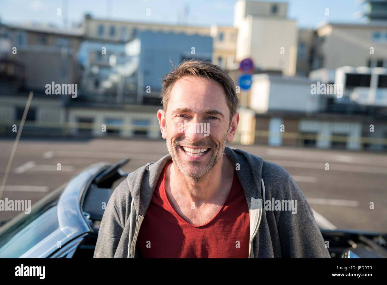 Ritratto di ridere uomo maturo con la stoppia nella parte anteriore della sua vettura sportiva Foto Stock