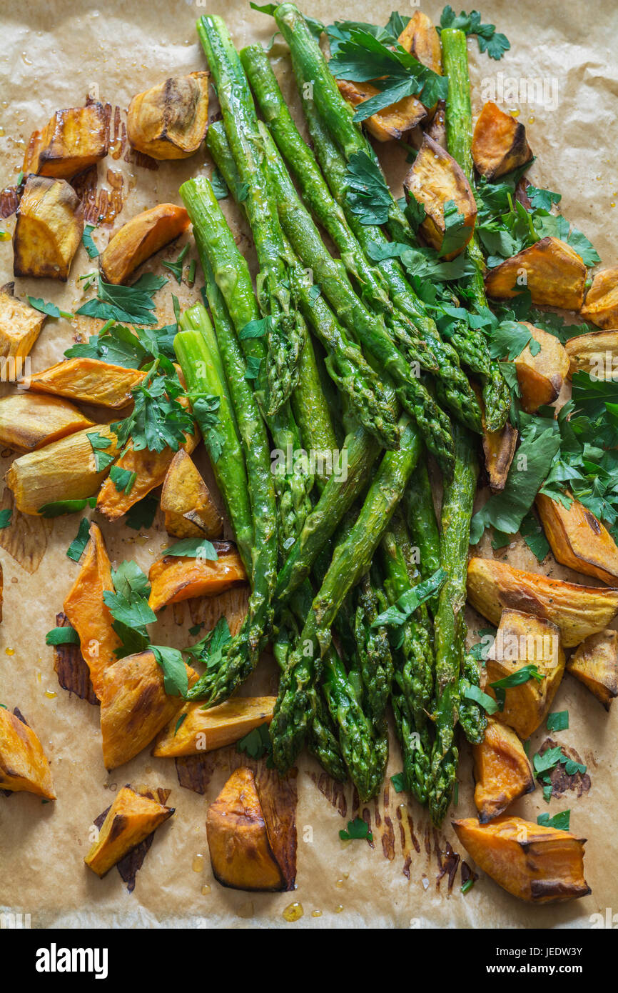 Cotta asparagi verdi, patate dolci e prezzemolo a foglia piatta sulla carta da forno Foto Stock