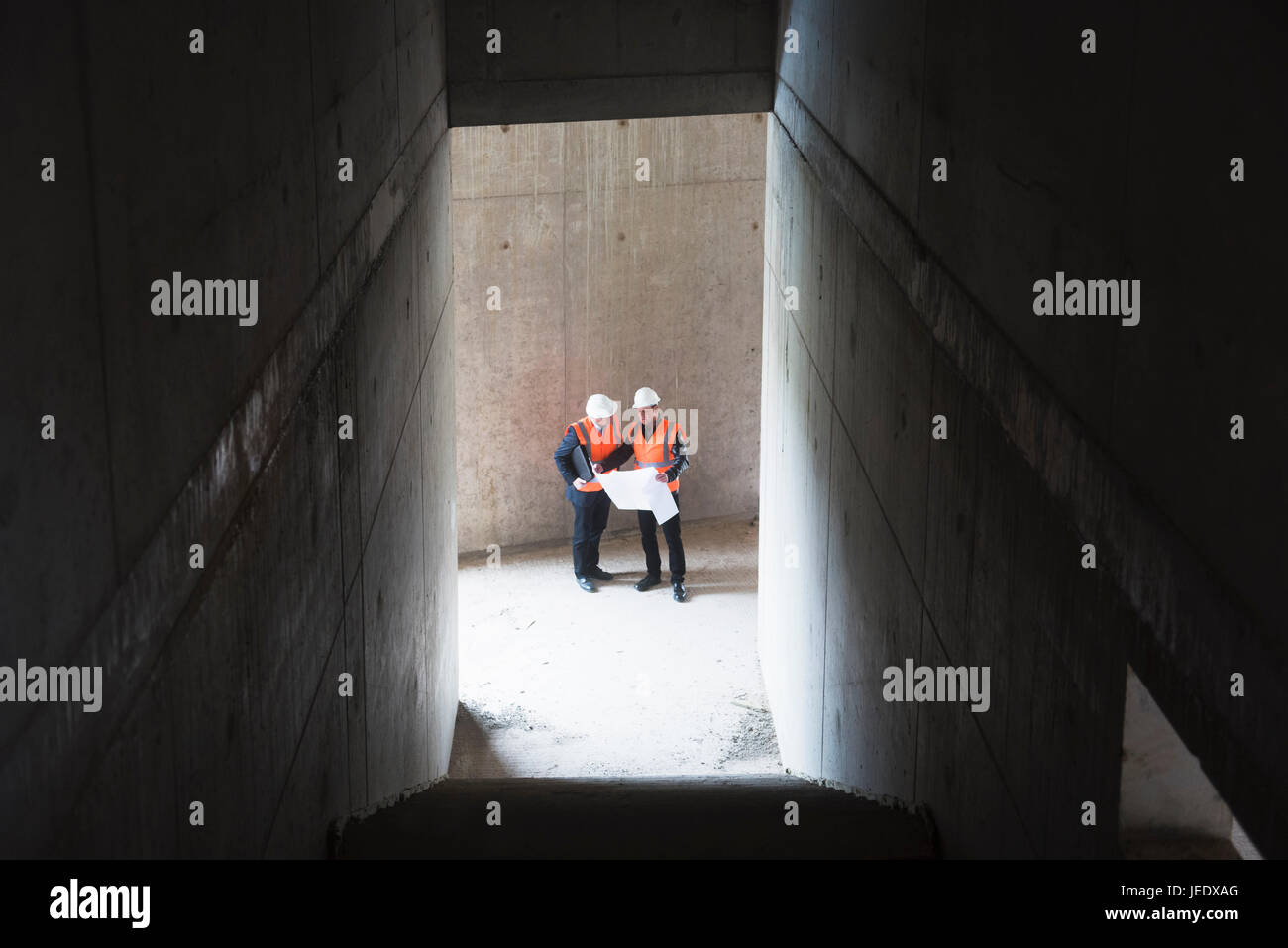Due uomini con il piano di indossare giubbotti di sicurezza parlando in edificio in costruzione Foto Stock