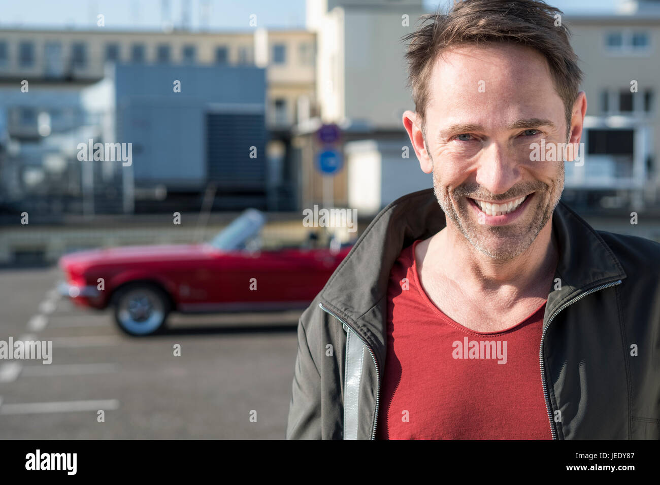 Ritratto di sorridere uomo maturo nella parte anteriore della sua vettura sportiva sul livello di parcheggio Foto Stock