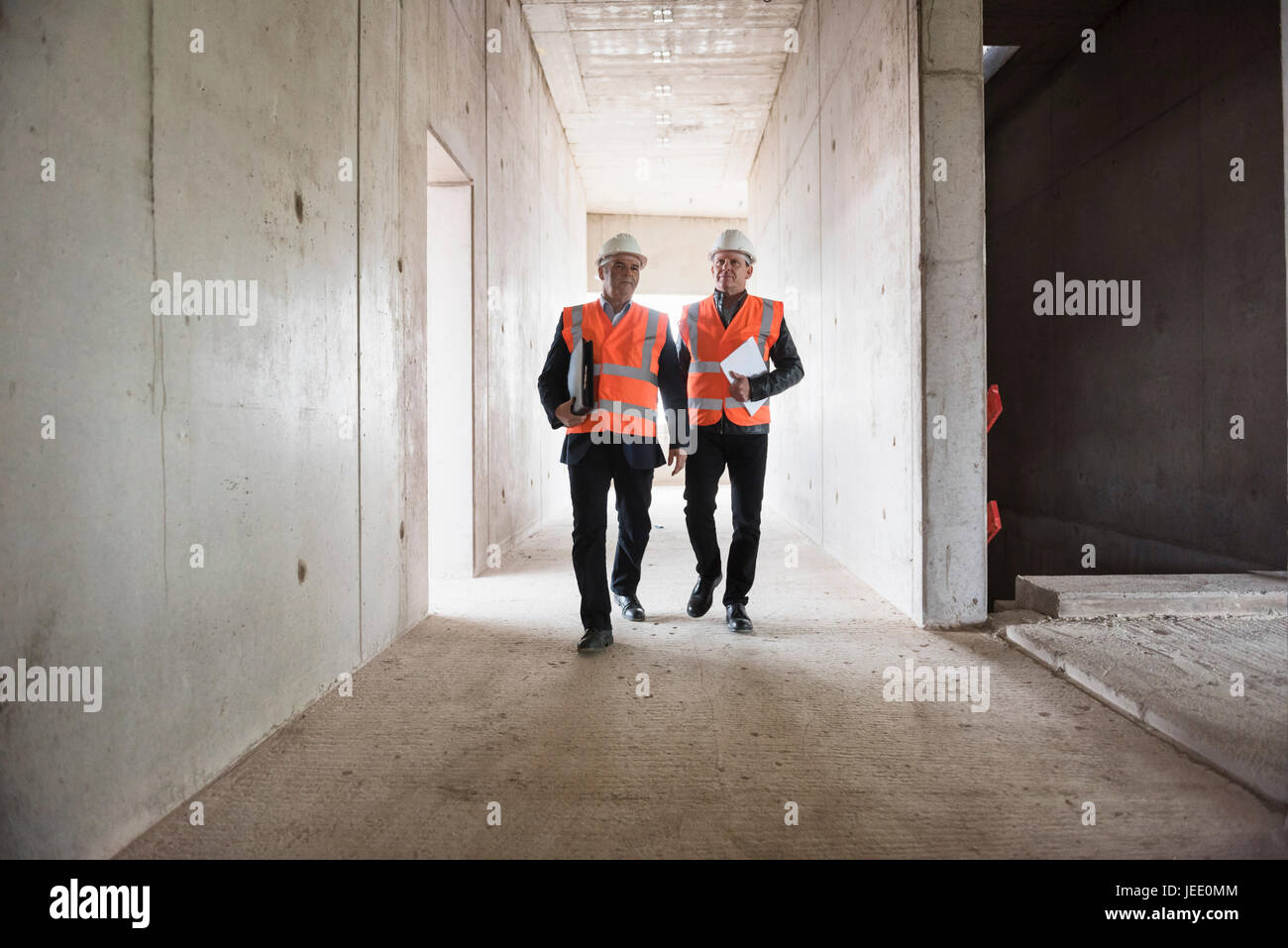 Due uomini che indossano la sicurezza a piedi in edificio in costruzione Foto Stock