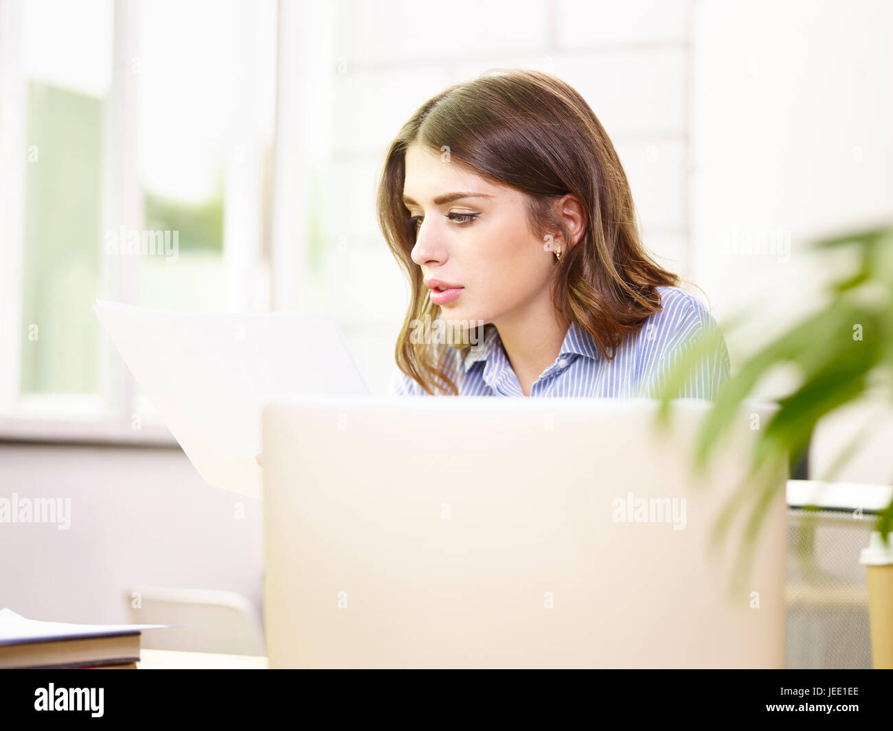 Giovane imprenditrice caucasica lavoro in ufficio guardando relazione mentre si utilizza il computer portatile. Foto Stock