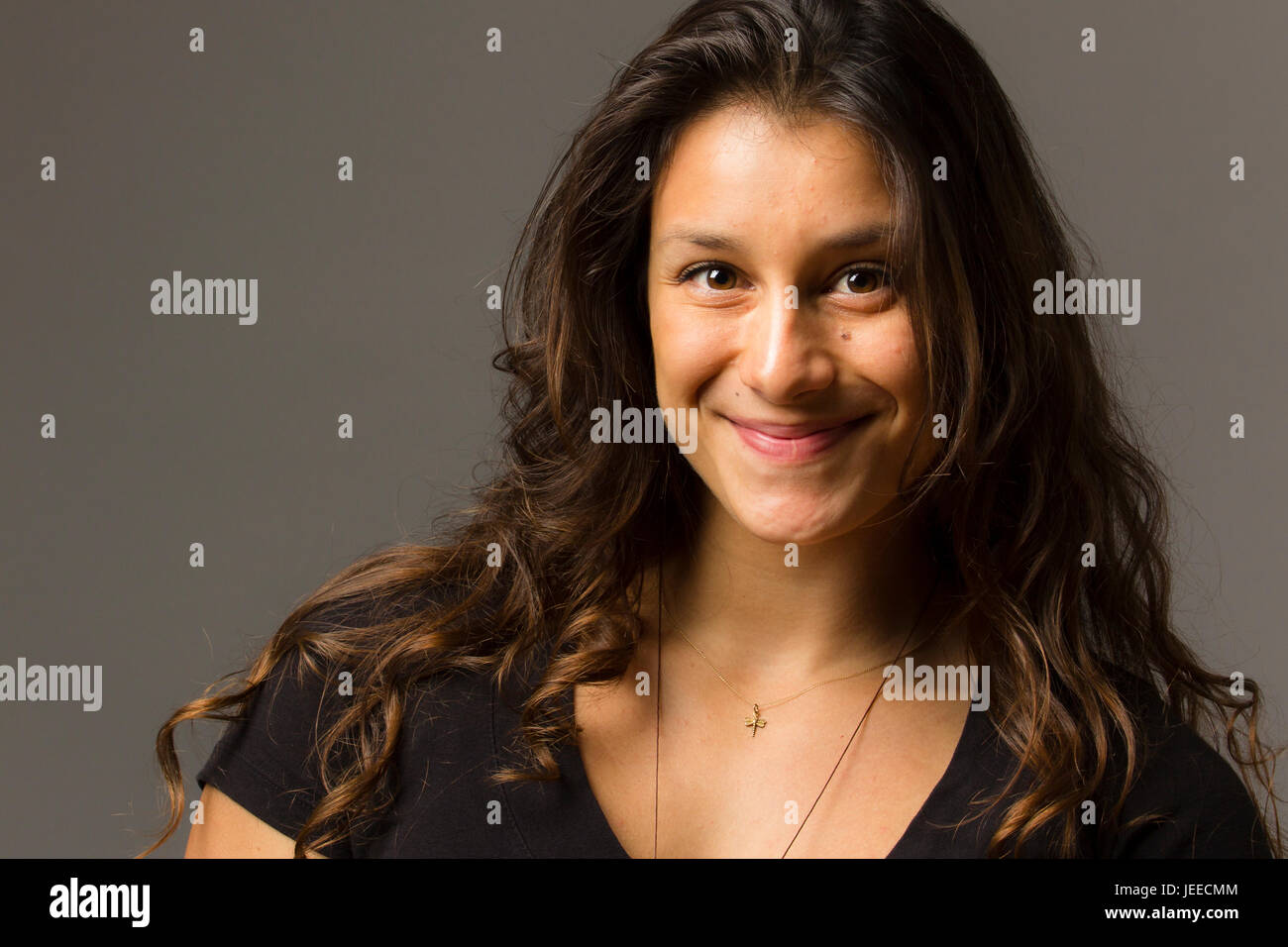 Giovani razza mista donna che indossa un nero di t-shirt e jeans sorge in pieno viso vista mentre sorridente al viewer Foto Stock