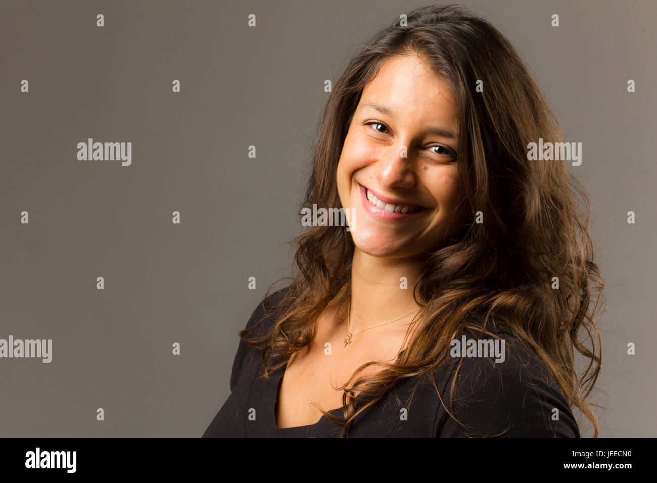 Giovani razza mista donna che indossa un nero di t-shirt e jeans sorge in pieno viso vista mentre sorridente al viewer Foto Stock