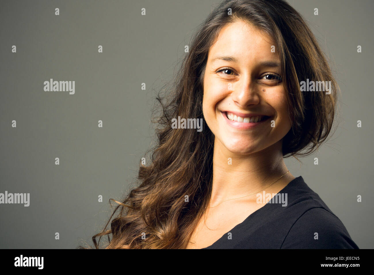 Giovani razza mista donna che indossa un nero di t-shirt e jeans sorge in pieno viso vista mentre sorridente al viewer Foto Stock