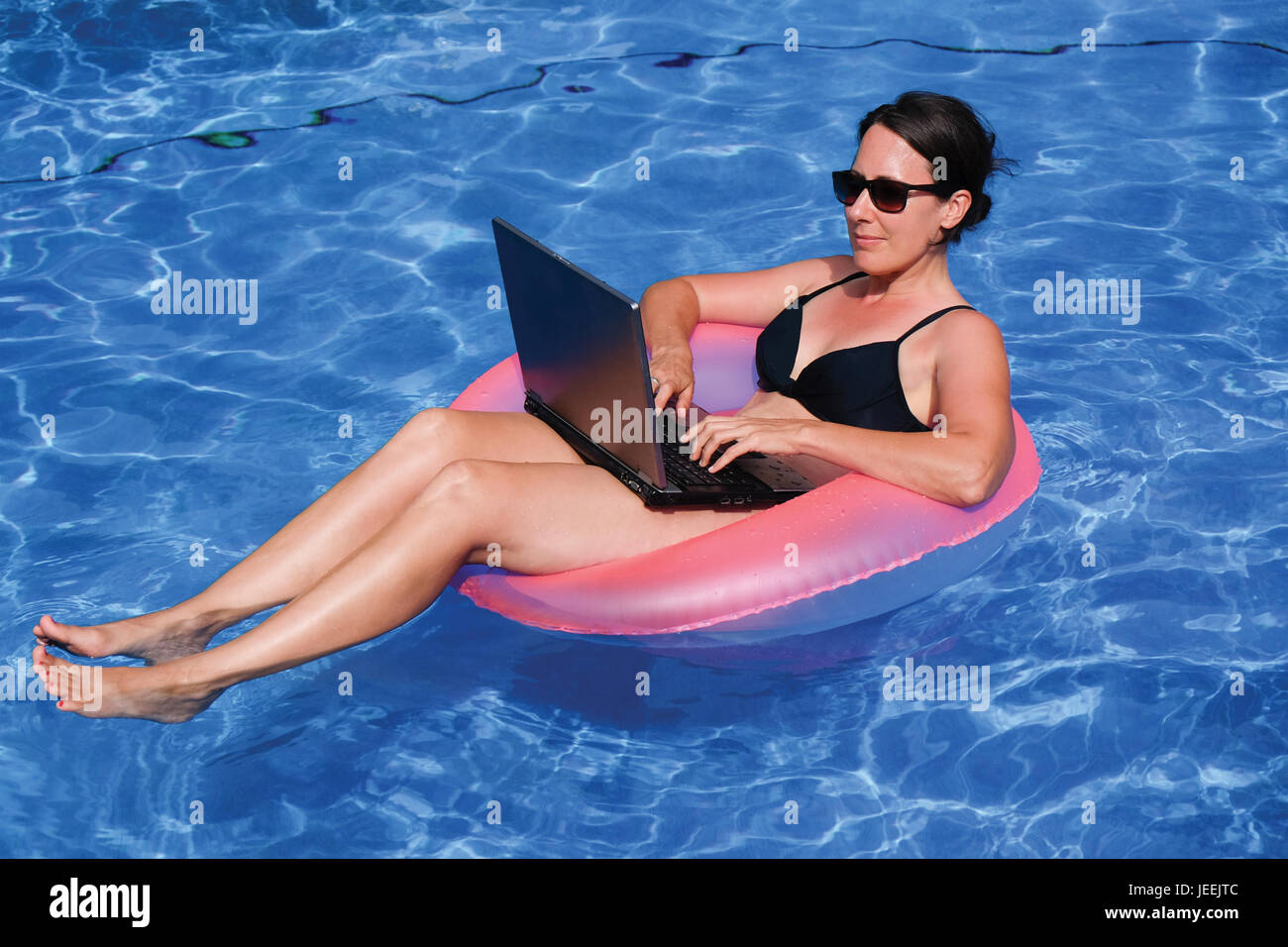 Di mezza età executive femmina del lavoro lavorando sul computer portatile in rosa gonfiabile di anello di vita in piscina in vacanza Foto Stock