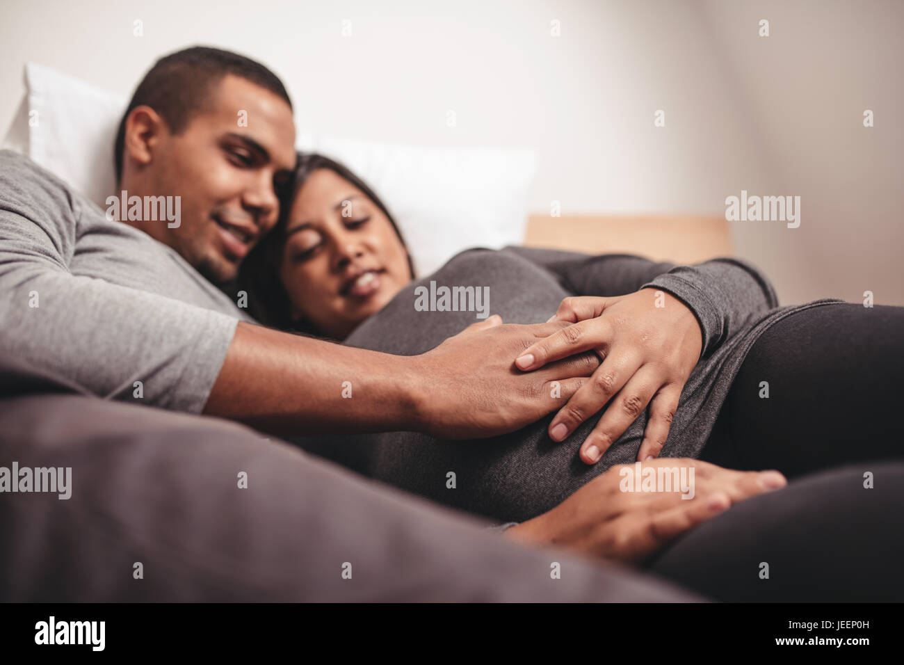 Giovane coppia incinta giacente sul letto di casa con le mani sulla pancia. Coppia giovane in attesa di un bambino. Foto Stock