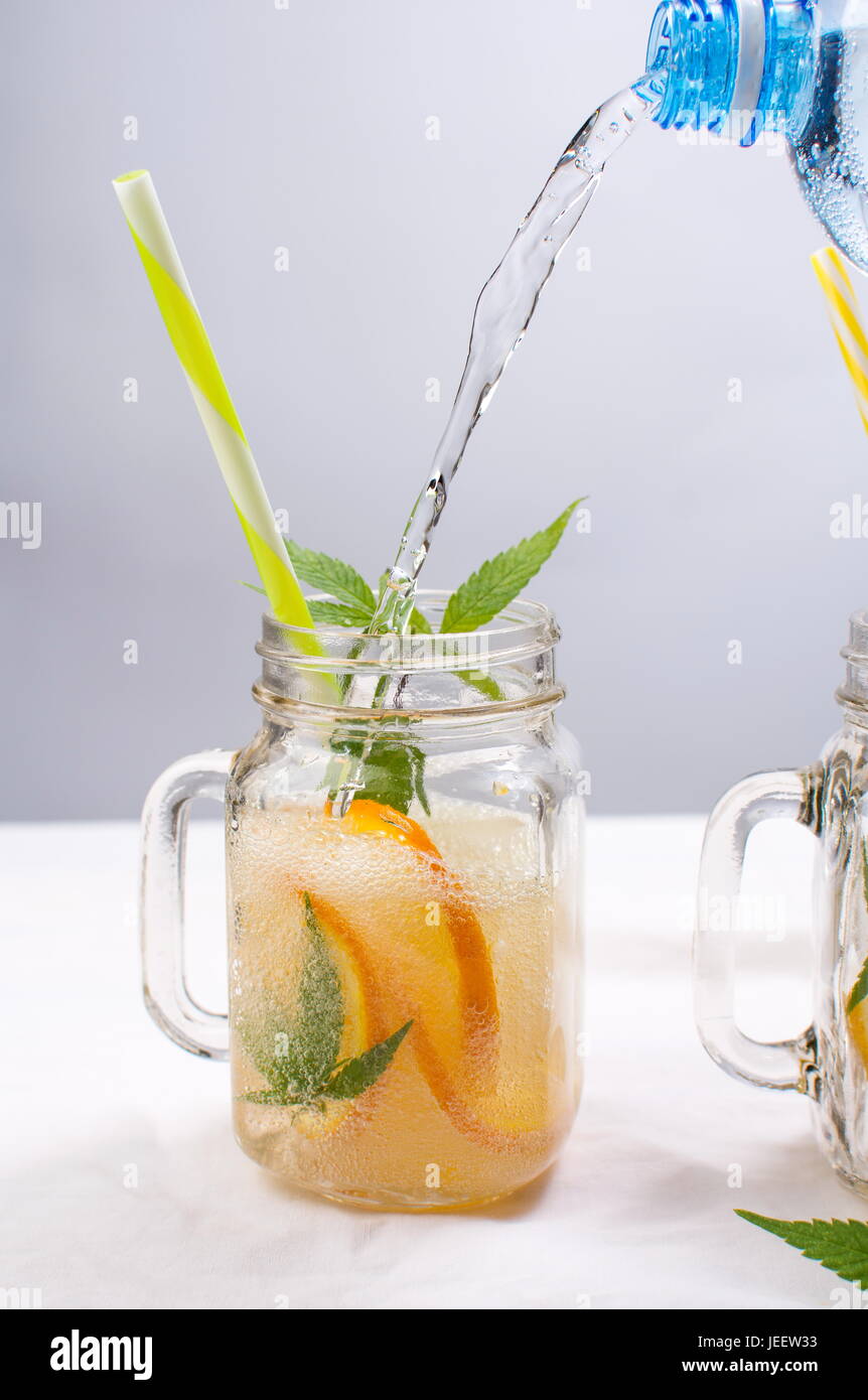 Versare acqua nel vaso con arancia e foglie di menta Foto Stock