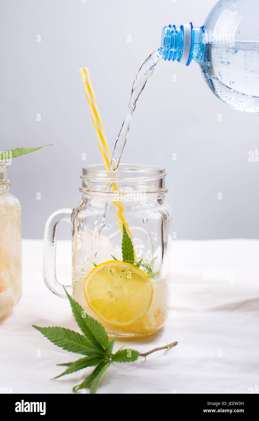 Versare acqua nel vaso con limone e foglie di menta Foto Stock