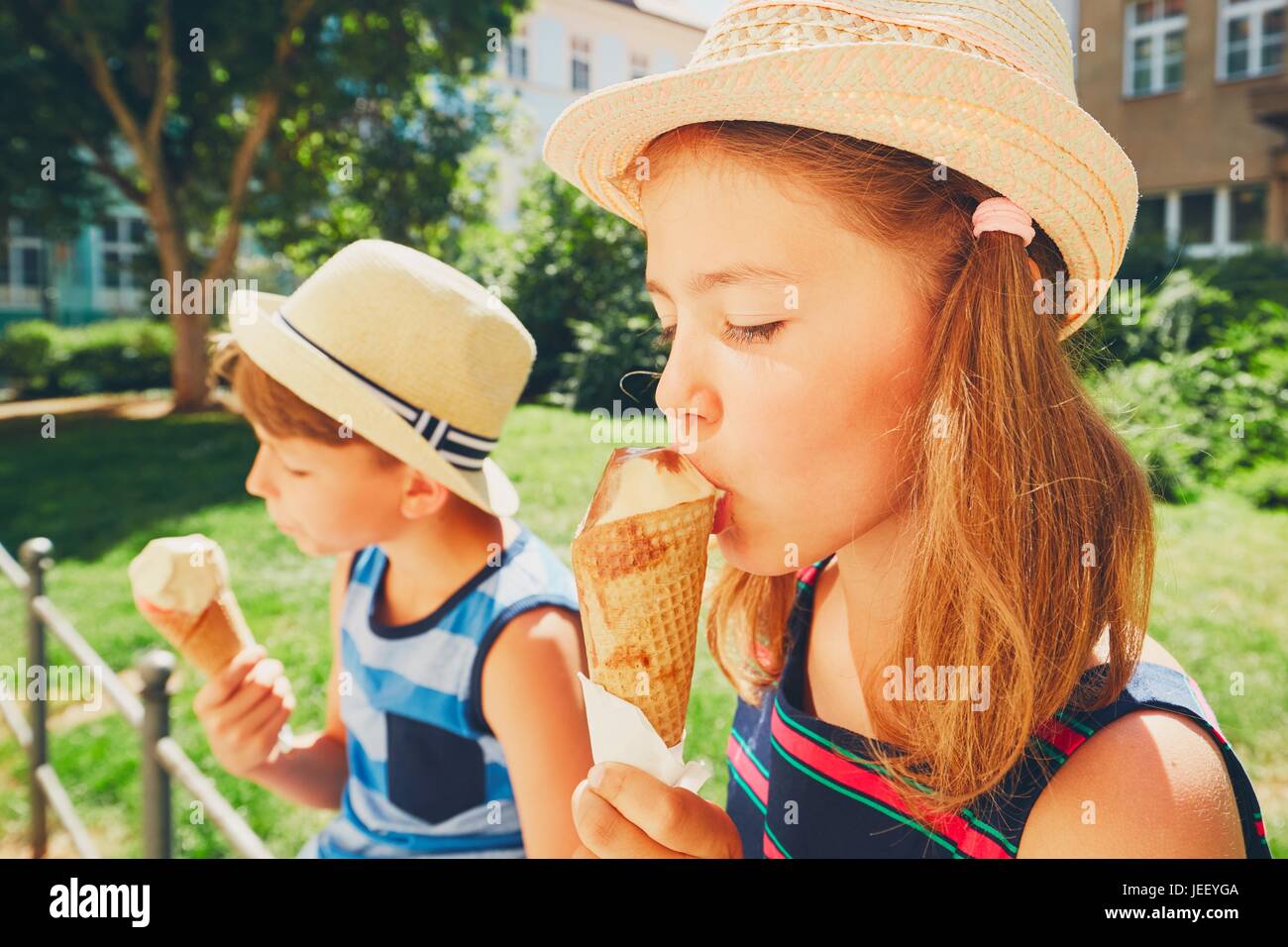 Giorno d'estate in città. Simpatici fratelli con cappelli grandi di mangiare il gelato nel parco. Foto Stock