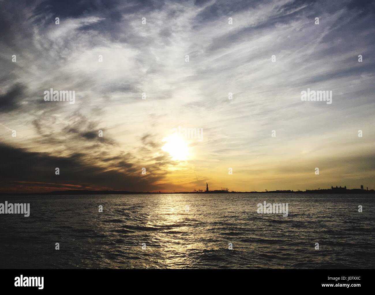 Statua della libertà su Liberty Island nel porto di New York al tramonto. Cielo spettacolare con nuvole dinamiche al tramonto. Lady Liberty in lontananza Foto Stock
