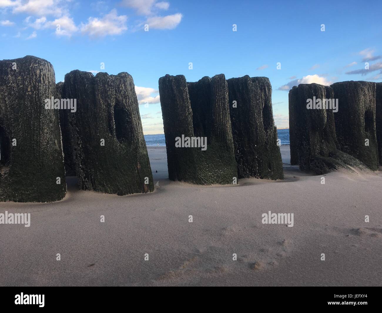 Silhouette di weathered posti di legno, i resti del molo in legno a Coney Island, New York. Spiaggia di sabbia e resti di legno del molo. Foto Stock