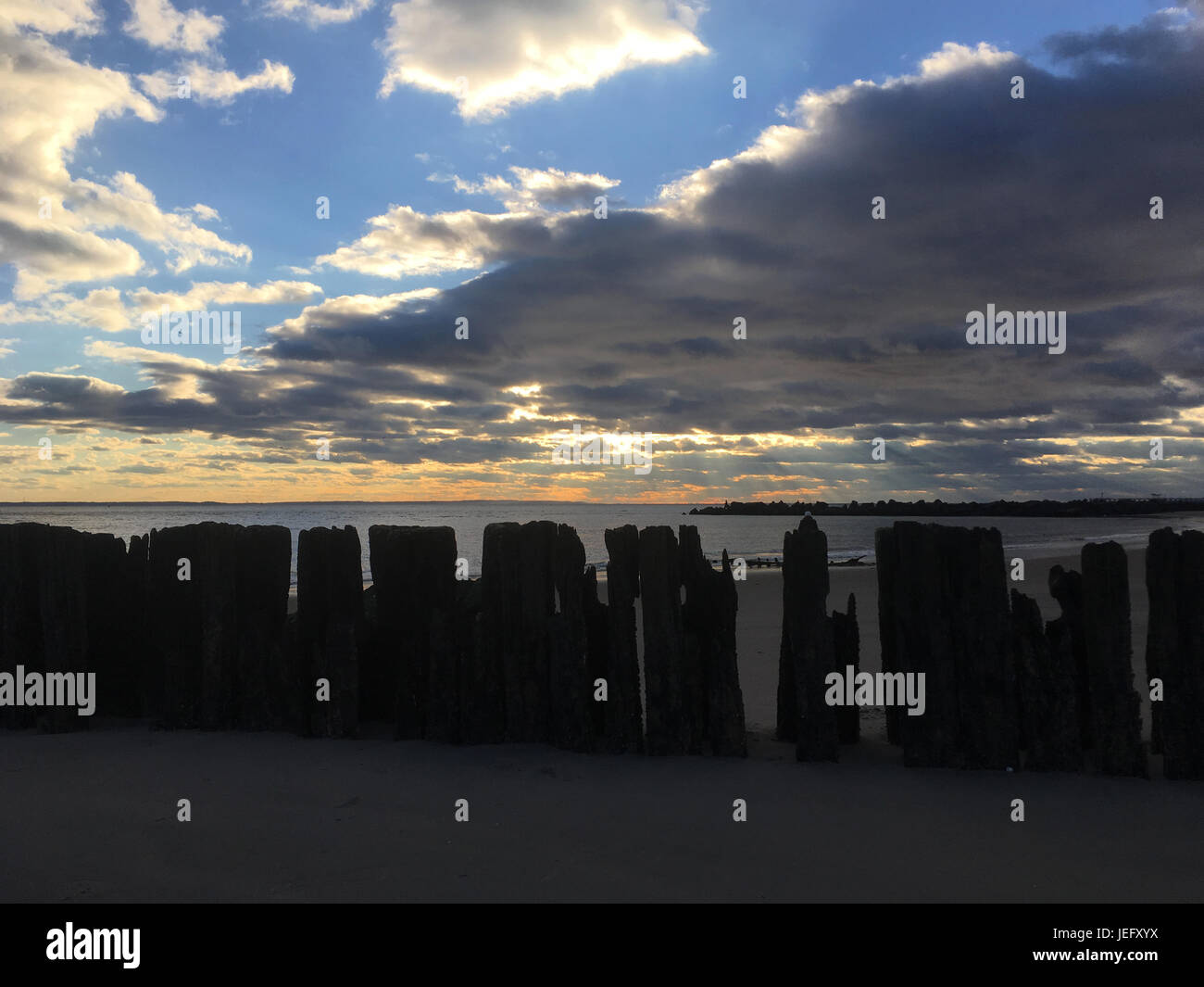 Fila di tralicci in legno da andato lungo molo sulla spiaggia di Coney Island, Brooklyn, New York. Tramonto spettacolare sulla spiaggia, puffy nuvole. Foto Stock