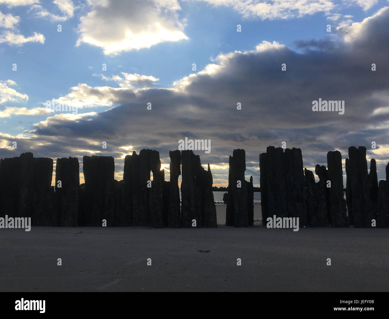Fila di vecchi posti di legno che utilizzato per il supporto di un molo in legno al tramonto. Cielo drammatico annuncio t tramonto con puffy nuvole. Coney Island, Brooklyn, New York. Foto Stock