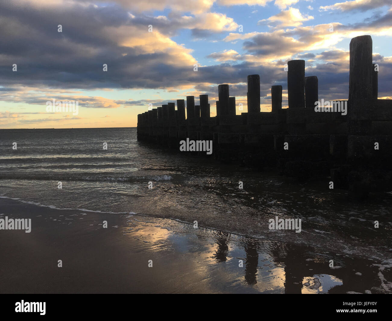 Nuvole drammatico al tramonto sull'oceano. Silhouette di un vecchio molo in legno in mare al tramonto, calma oceano onde spazzola contro la spiaggia sabbiosa. Foto Stock