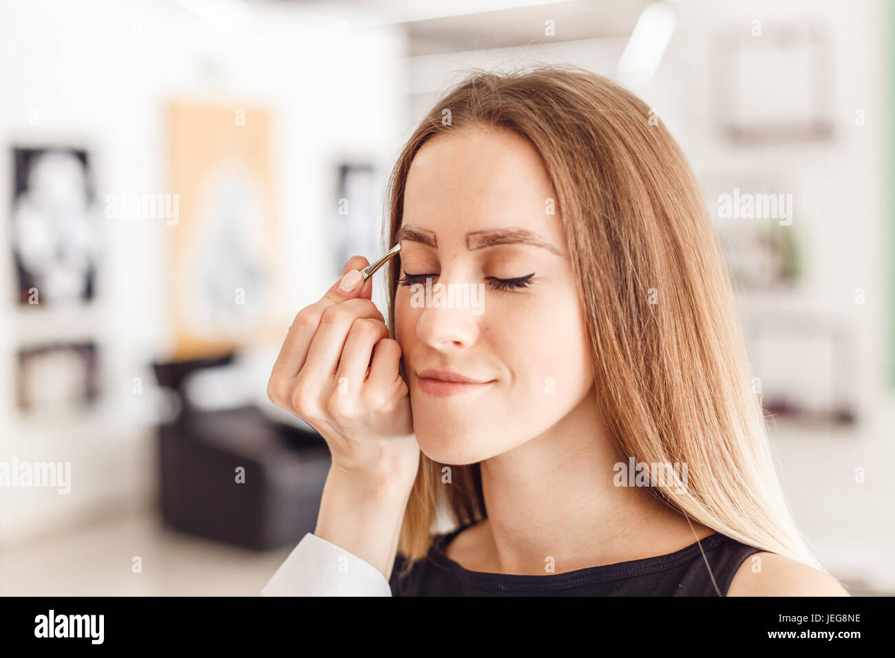 Giovane donna tweezing le sopraciglia nel salone di bellezza. Foto Stock