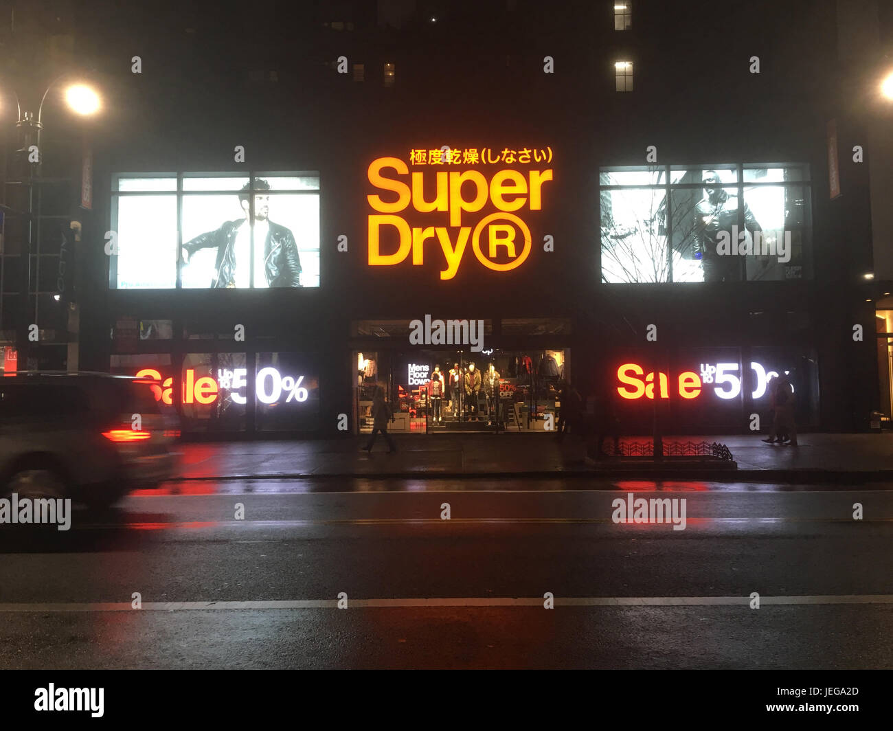 New York City - 20 gennaio 2017: Superdry, rivenditore di abbigliamento giapponese, a Midtown New York di notte dopo la pioggia. Luci di posizione posteriori per auto dei veicoli che passano. Foto Stock