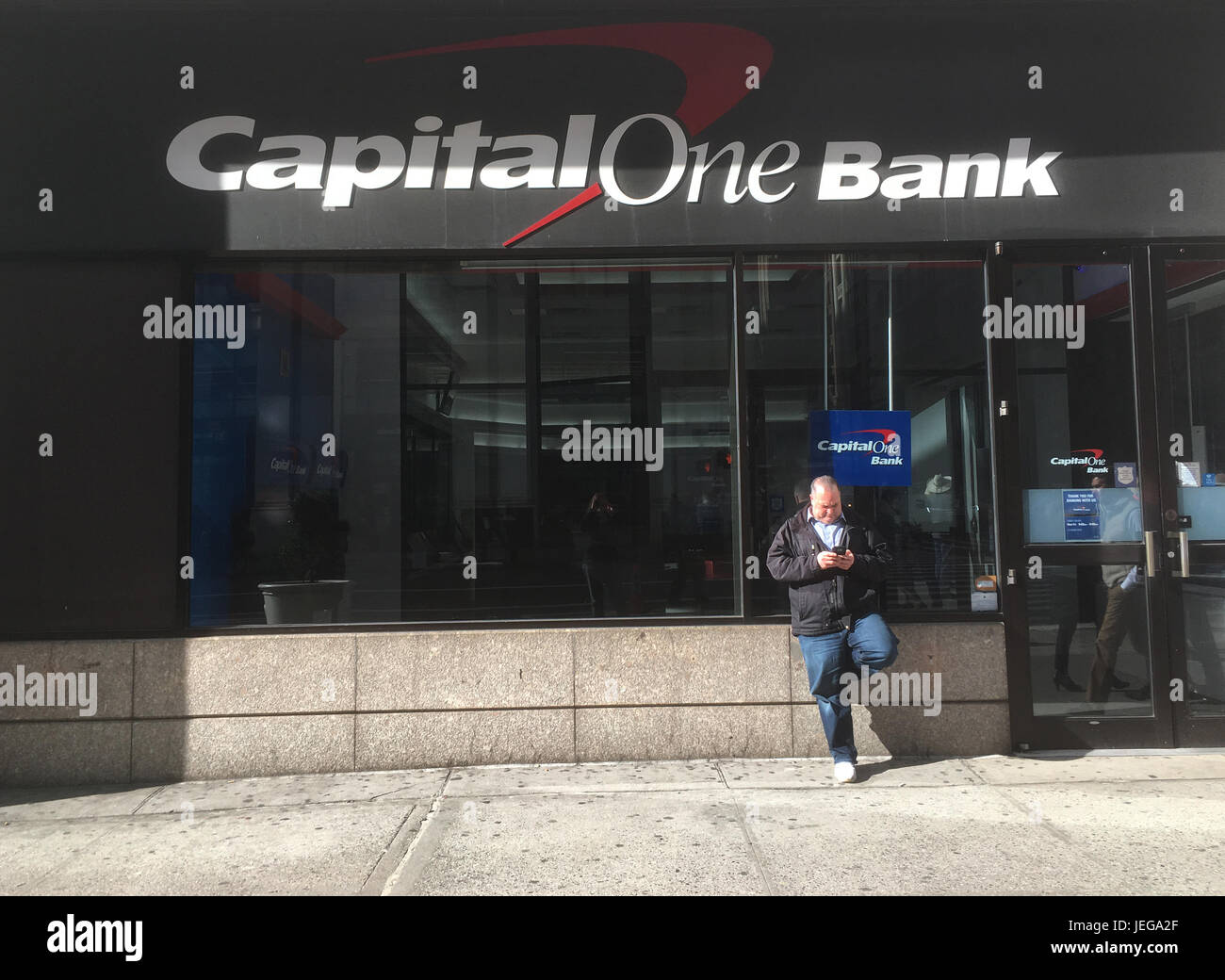 New York City - 28 Gennaio 2017: Uomo in felpa con cappuccio si appoggia contro una parete guardando il telefono davanti di capitale in una banca di Midtown Manhattan, New York. Foto Stock