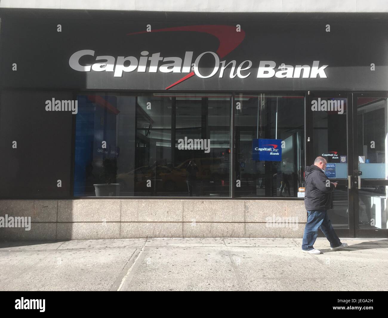 New York City - 28 gennaio 2017: L'uomo grasso corto guarda il suo telefono mentre cammina passato la banca di capitale uno nella filiale di New York City Midtown Manhattan. Foto Stock