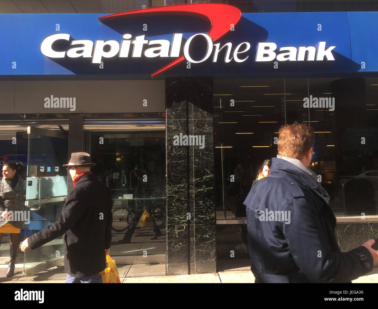 New York City - 28 Gennaio 2017: donna lascia la banca, l'uomo in una fedora e un paio a piedi passato la capitale in una banca di Midtown Manhattan su 6h Avenue o Foto Stock