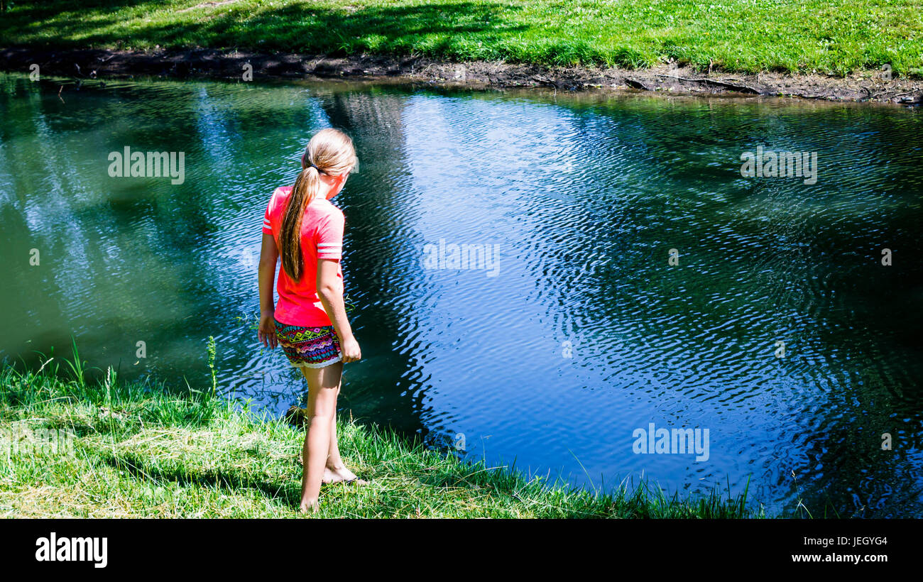 Bambina guardando il pesce in un piccolo stagno Foto Stock