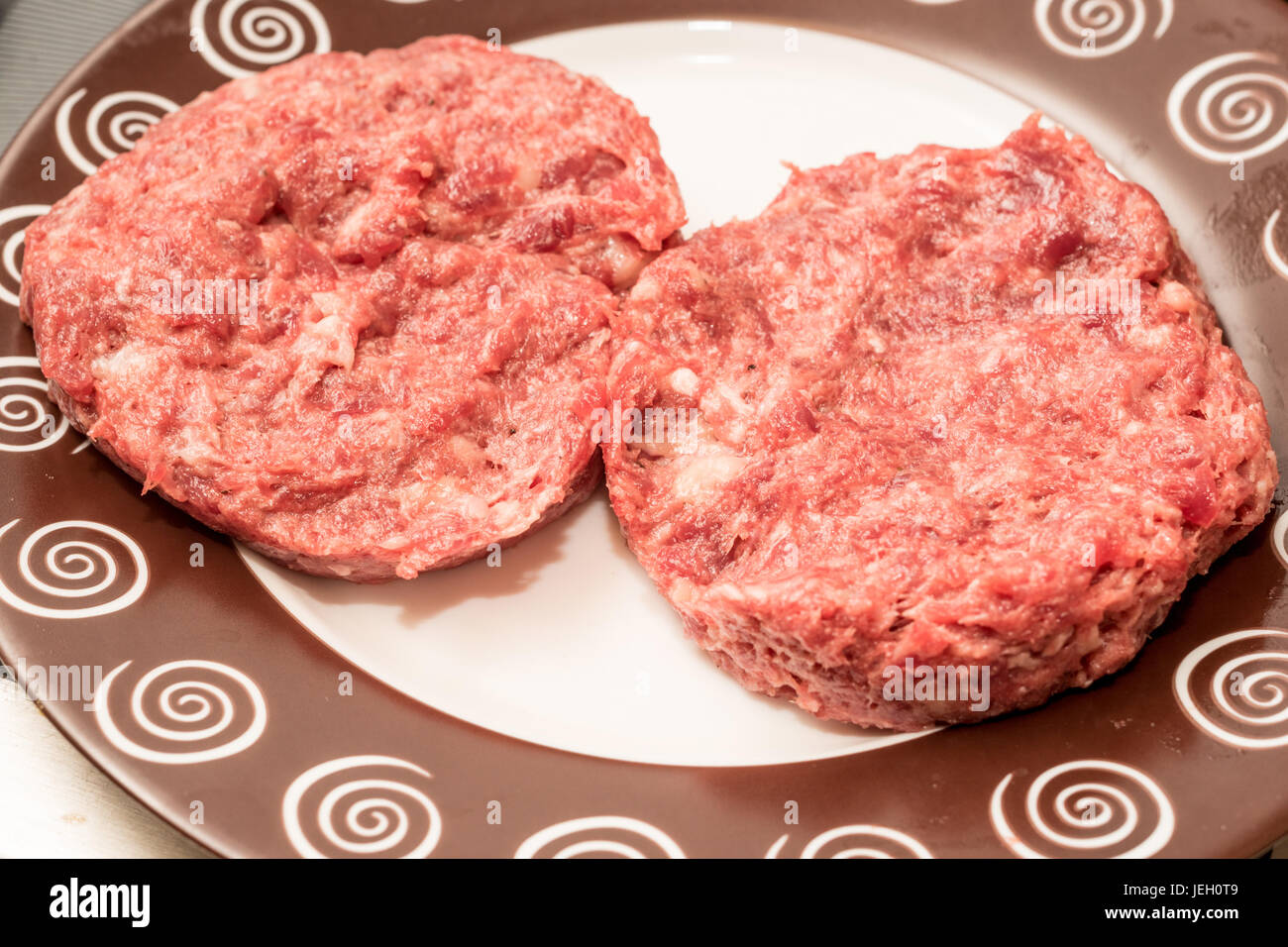 Crudo fresco carni bovine gli hamburger sulla piastra Foto Stock