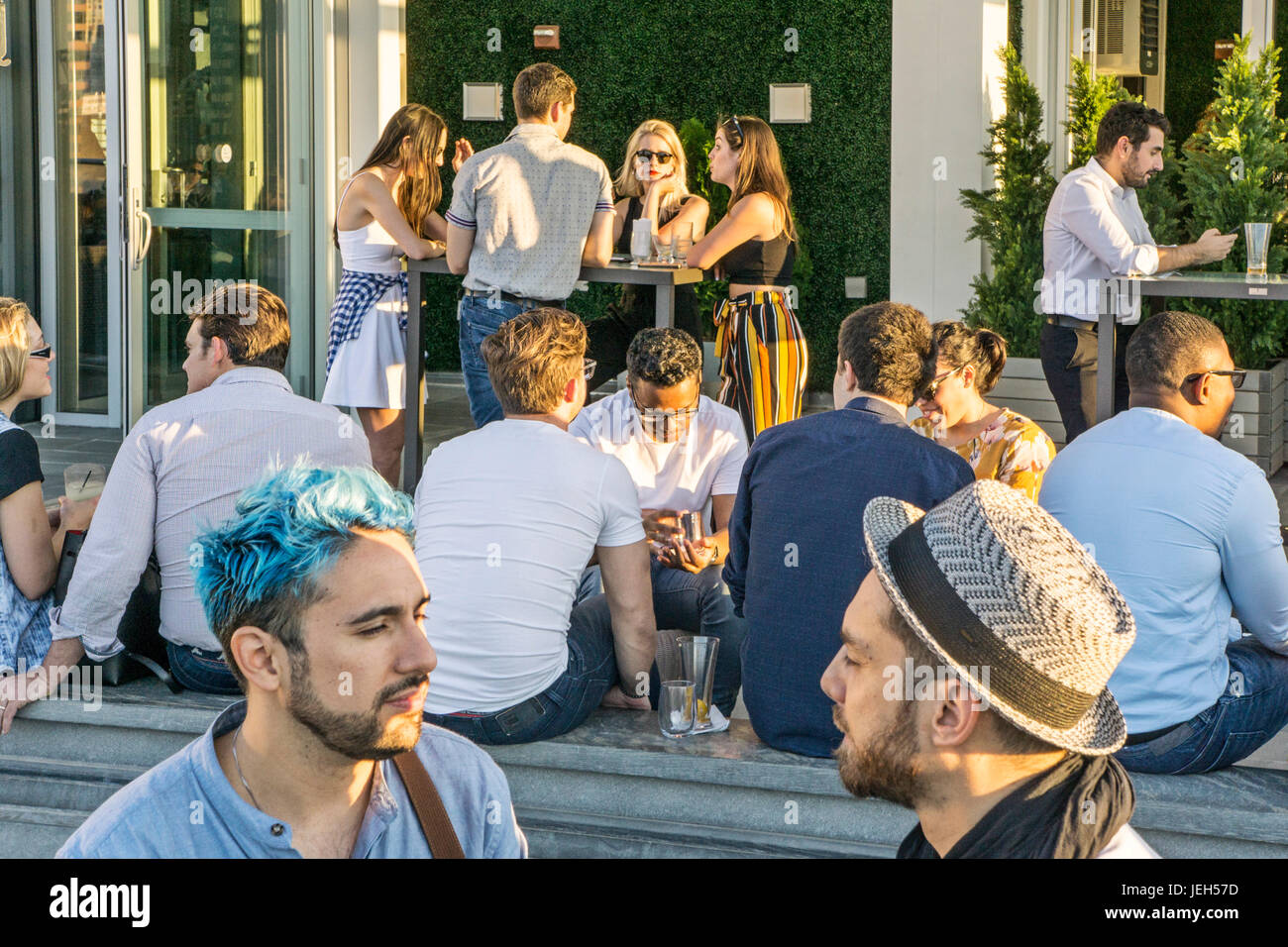 Diversi gruppi di giovani e dorato da sole di setting godere di socializzazione tra cui coppia gay, uno con colorazione blu nei suoi capelli Ink48 hotel bar sul tetto Foto Stock