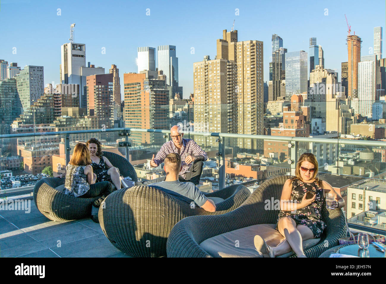 Persone a Ink48 hotel rooftop bar angolo godendo di appollaiarsi su ammortizzata rattan divani e sedie con vista al di là dello skyline di Hells Cucina illuminata dal sole di setting Foto Stock