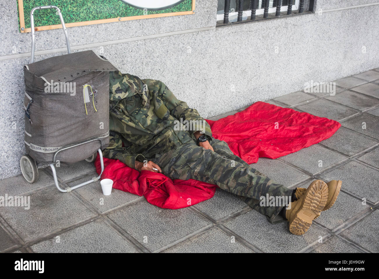 Senzatetto dormire in strada con la sigaretta accesa in mano. Foto Stock