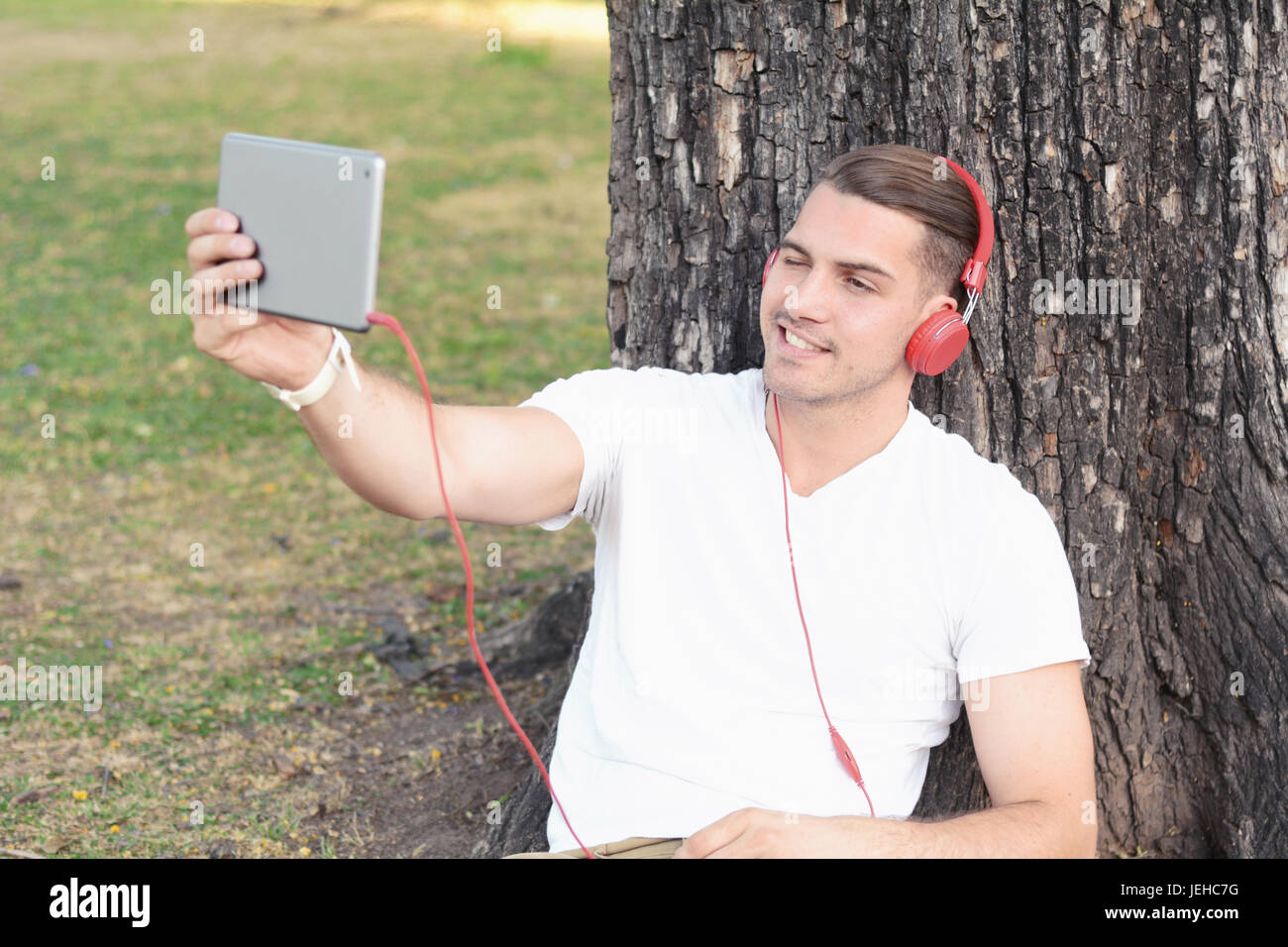 Ritratto di un giovane uomo latino tenendo un selfie con tavoletta digitale. All'esterno. Foto Stock