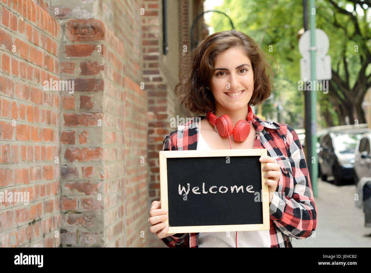 Giovane donna bellissima azienda lavagna con il testo "benvenuto". All'esterno. Foto Stock