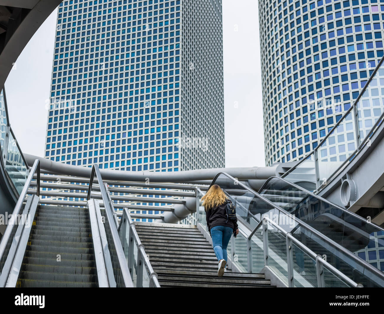 Una donna cammina su per le scale con una vista della torre quadrata e la torre circolare del centro Azrieli; Tel Aviv, Israele Foto Stock