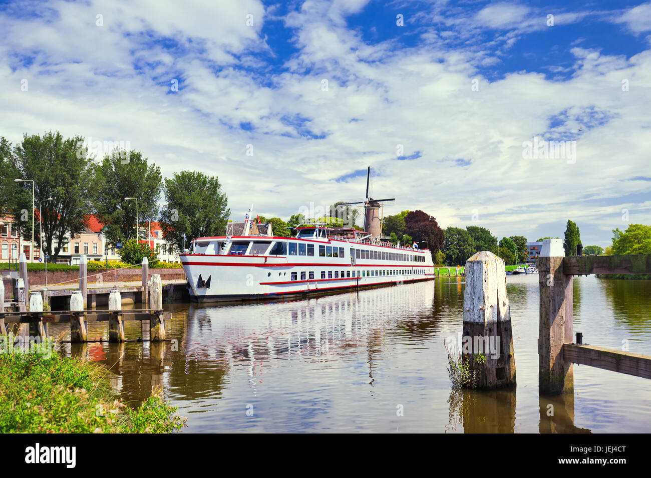 White tour-barca ormeggiata in un tranquillo canale con un mulino a vento sullo sfondo, Gouda, Paesi Bassi Foto Stock