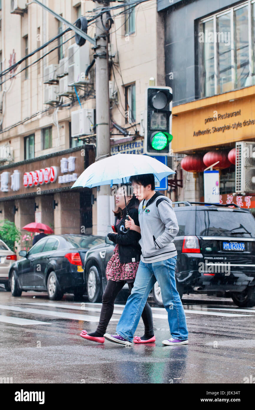 Coppia cinese con ombrellone attraversa street. Shanghai è un umido clima subtropicale con occasionali acquazzoni o temporali. Foto Stock