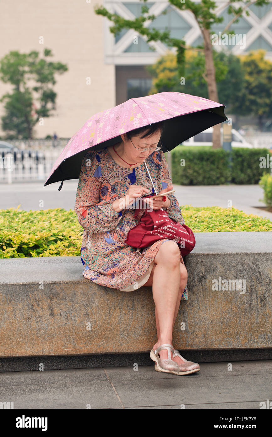 PECHINO-16 GIUGNO 2015. Donna di mezza età in un parco occupato con il suo smartphone in una giornata di sole. Foto Stock