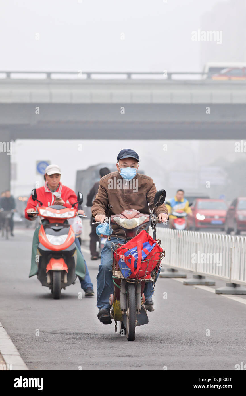 PECHINO-PTOM. 11 ,2014. Vecchio uomo in bicicletta elettrica in città coperta smog. Una concentrazione di PM2,5, piccole particelle che pone un rischio enorme per la salute. Foto Stock