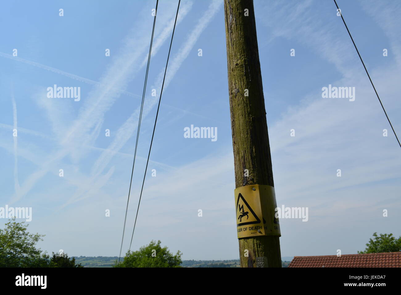 Le linee di alimentazione e del pericolo di morte un cartello di segnalazione sull elettricità in legno post pilone con vapore sentieri nel cielo Herefordshire England Regno Unito Foto Stock