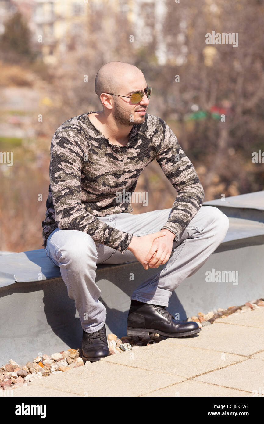 Uomo in occhiali da sole seduto su una parete Foto Stock