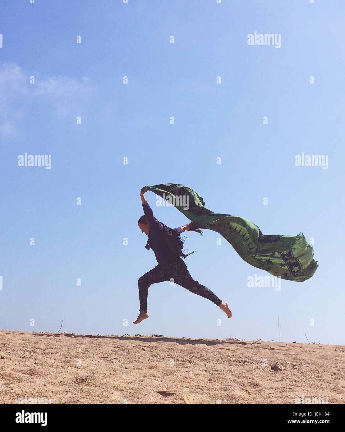 Donna sulla spiaggia jumping, tenendo una sciarpa Foto Stock