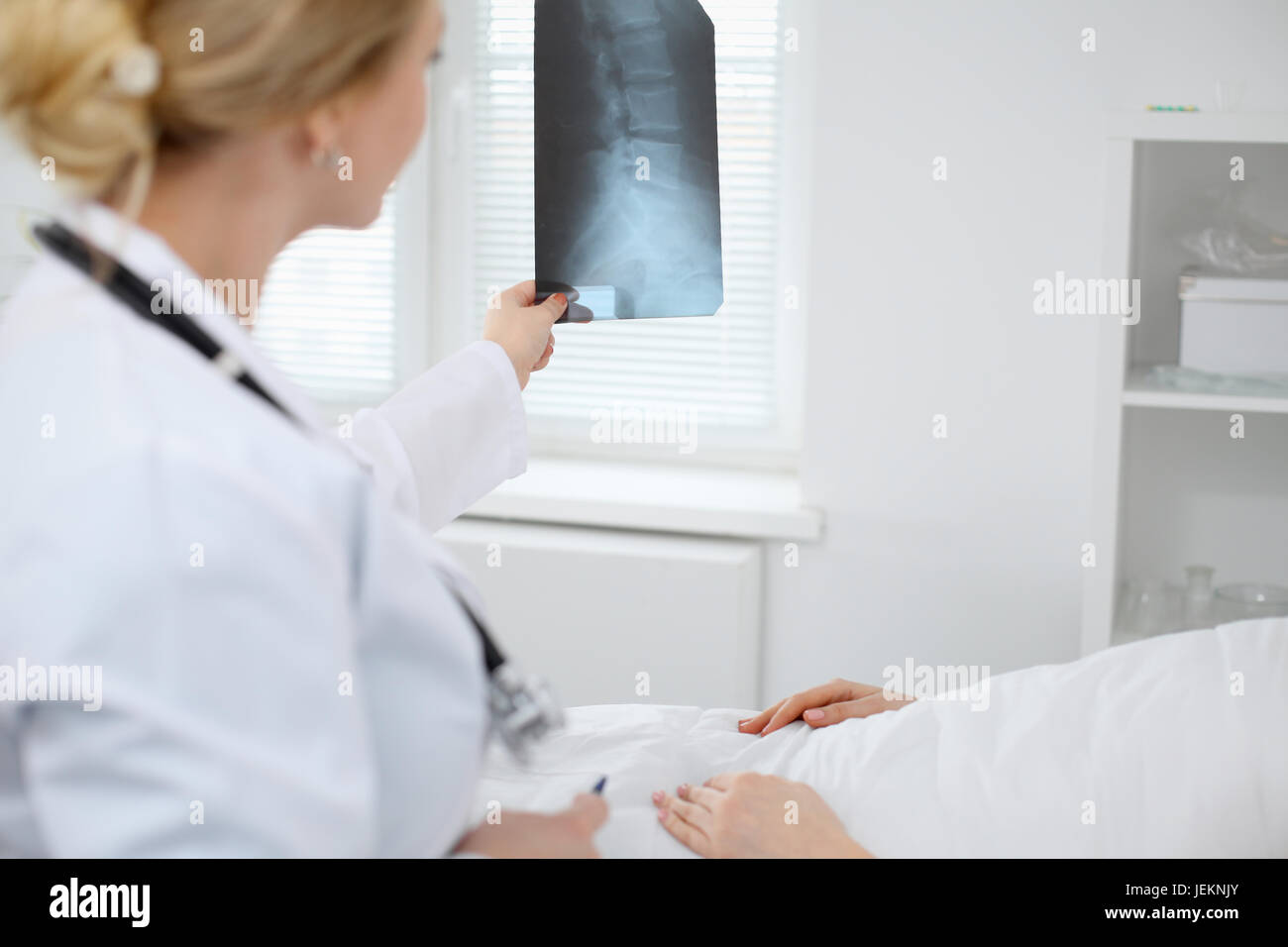 Medico donna esamina un X-ray immagine della colonna vertebrale accanto al paziente sdraiato sul letto in ospedale. Foto Stock